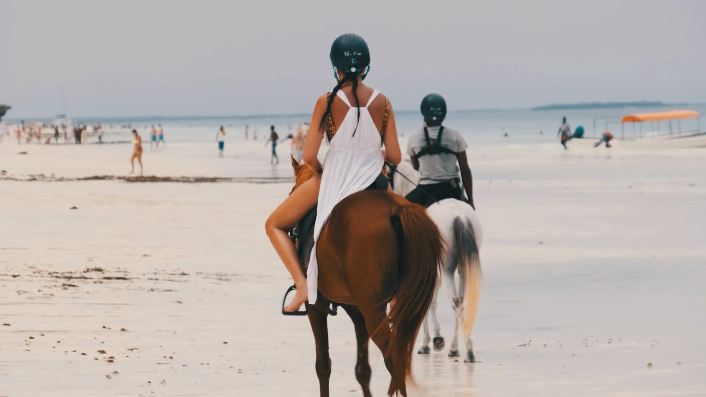Horse riding along a white-sand beach at low tide